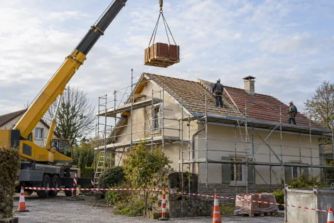 Grue levant une palette de tuiles au-dessus d’une toiture en chantier — illustration